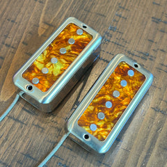 Two filtertron guitar humbucker pickups with amber tortoiseshell-patterned coils, displayed on a dark wood surface.
