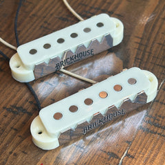 Two Brickhouse guitar jaguar pickups with cream-colored covers resting on a wooden surface.